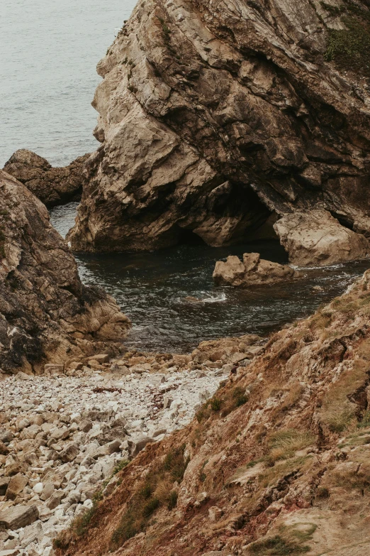 a man standing on top of a cliff next to a body of water, inspired by Elsa Bleda, romanticism, crazy looking rocks, unsplash 4k, marble hole, pembrokeshire