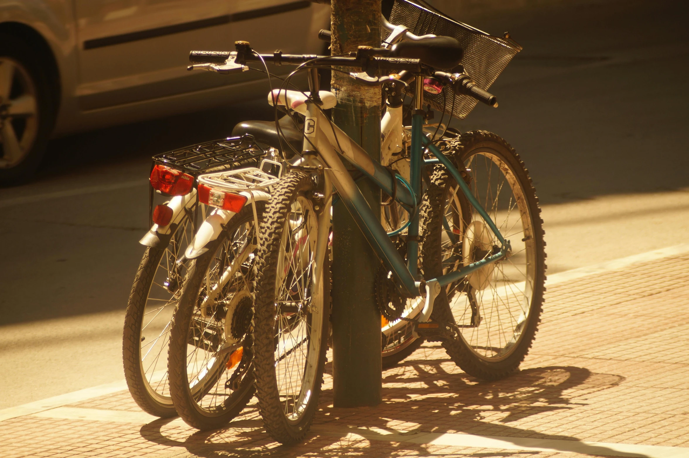 a couple of bikes are chained to a pole, sun dappled, cycles4d, spanish, fully functional