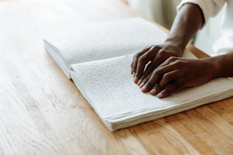 a person reading a book on a wooden table, private press, riyahd cassiem, hand on table, language, thumbnail