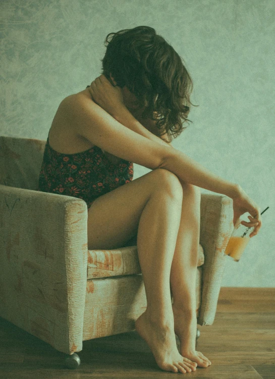 a woman sitting in a chair on a hard wood floor, a picture, inspired by Elsa Bleda, pexels, portrait of depressed teen, with a drink, ilustration, hugging her knees