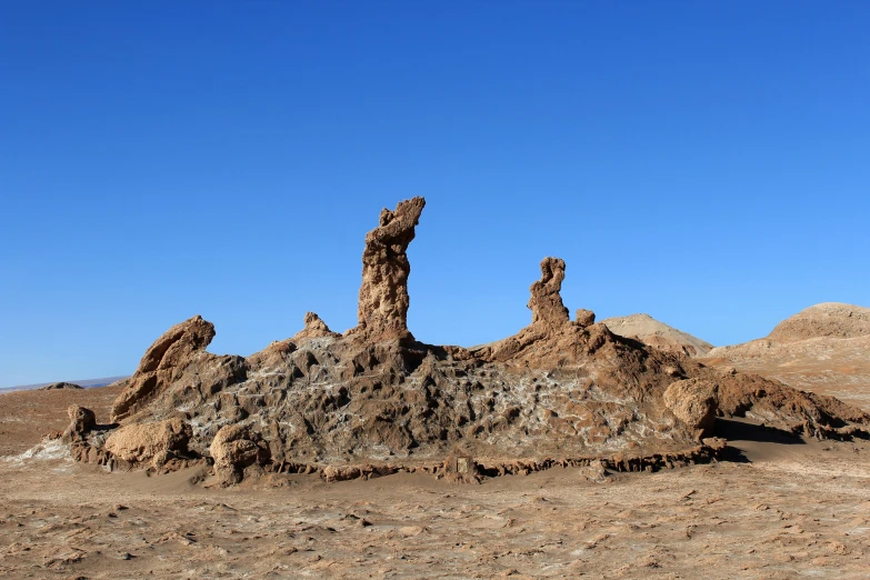 a rock formation in the middle of a desert, a surrealist sculpture, unsplash, land art, blue sky, chile, three towers, anthropology photo”