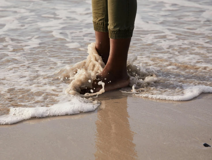 a person standing on top of a beach next to the ocean, by Nina Hamnett, unsplash, wet feet in water, lined in cotton, tan complexion, pouring