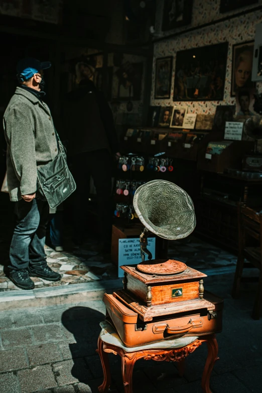 a man standing next to a pile of luggage, an album cover, trending on pexels, kinetic art, inside an old magical shop, street photo, speakers, carrying a tray