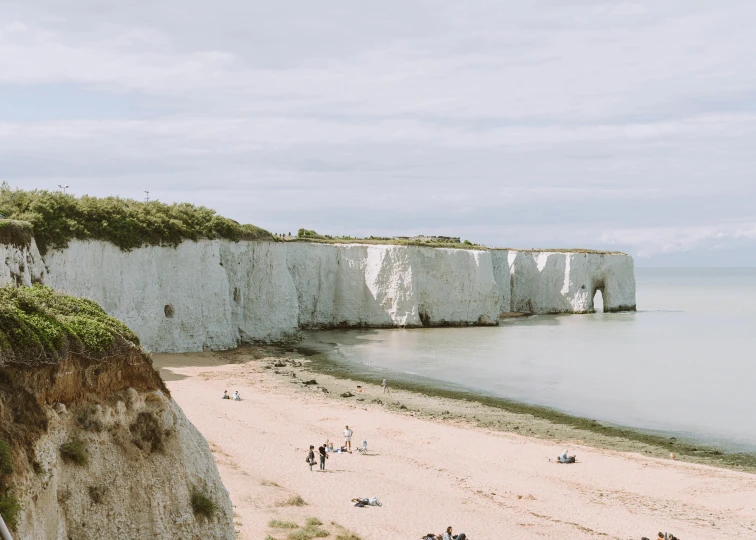 a group of people standing on top of a sandy beach, by Rachel Reckitt, pexels contest winner, chalk cliffs above, white concrete, byzantine, slightly pixelated