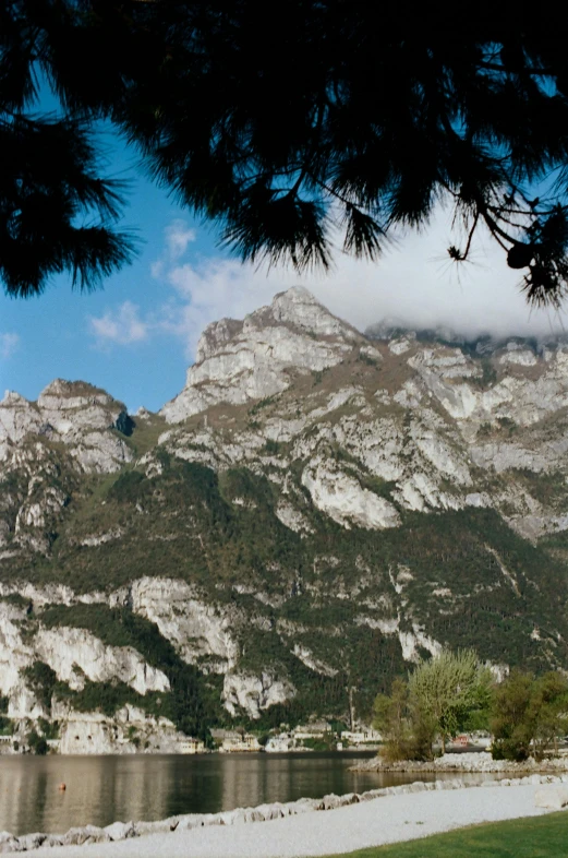 a bench next to a body of water with mountains in the background, a picture, les nabis, face looking skyward, limestone, with dark trees in foreground, peaks