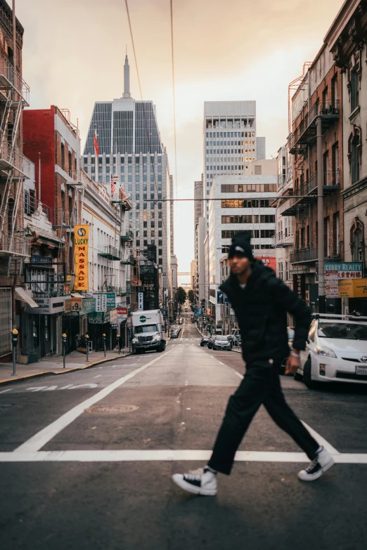 a man crossing a street in the middle of a city, pexels contest winner, bay area, at full stride, wearing jeans and a black hoodie, buildings in the distance
