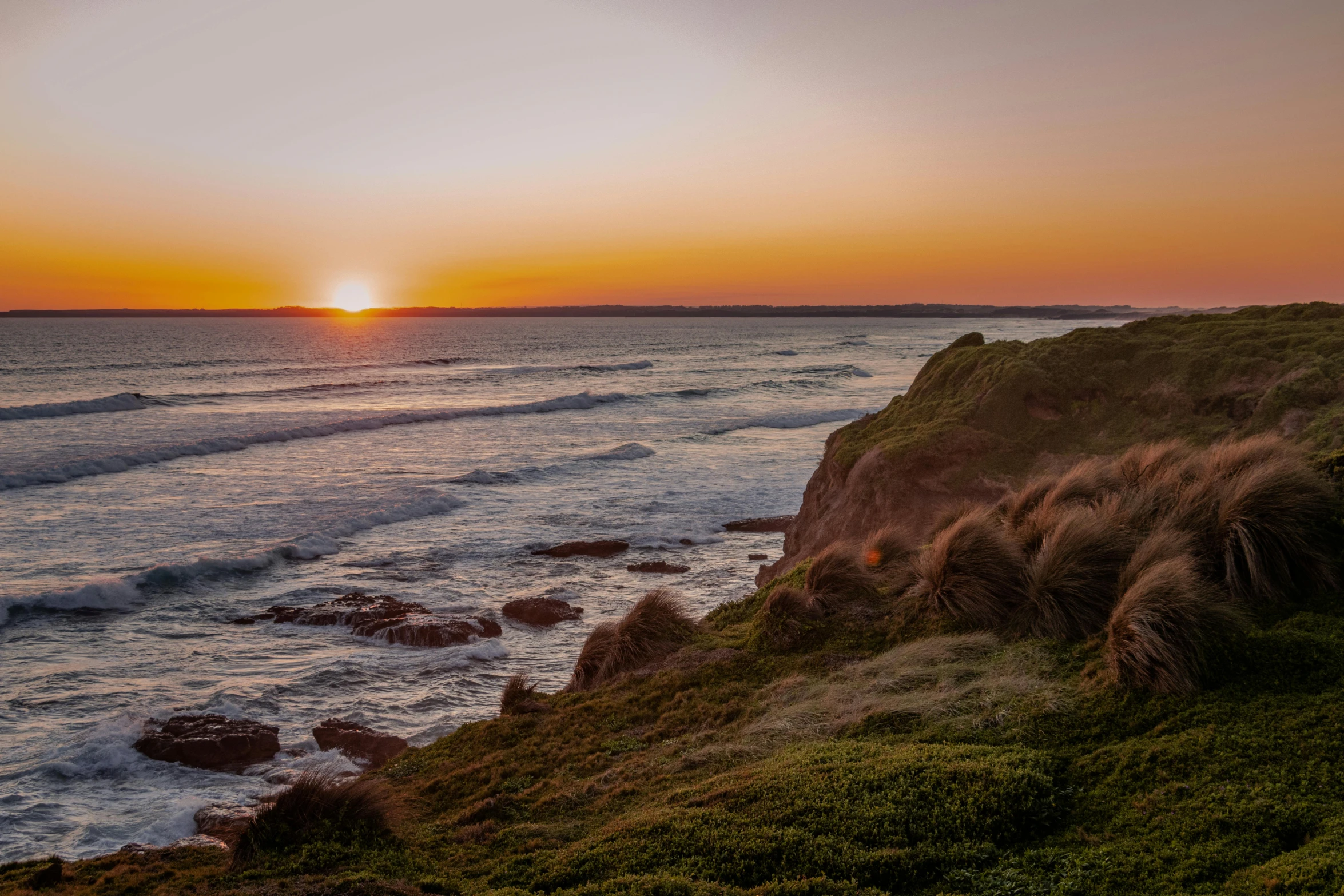 a lighthouse sitting on top of a cliff next to the ocean, by Peter Churcher, pexels contest winner, sunset panorama, manuka, grass and rocks, distant photo