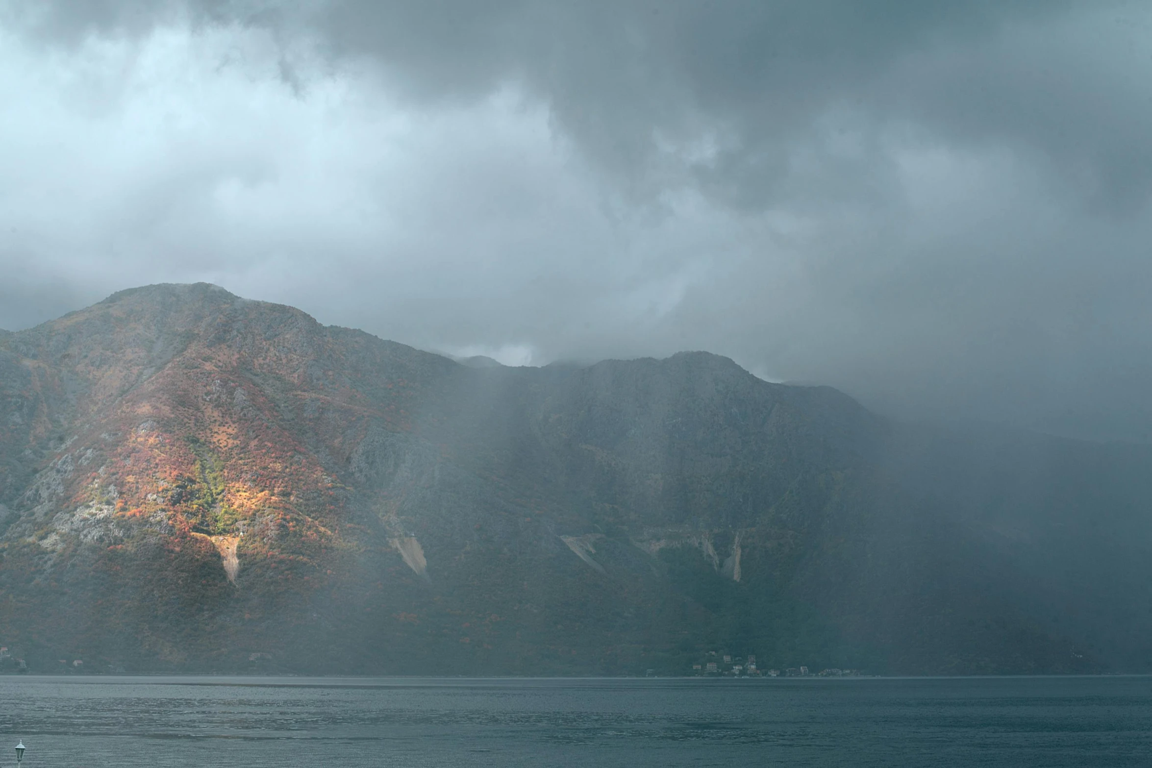 a large body of water with a mountain in the background, by Jens Søndergaard, pexels contest winner, hurufiyya, rain lit, autumn light, boka, steep cliffs