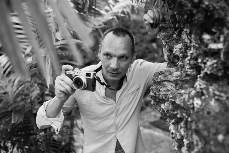 a black and white photo of a man holding a camera, a black and white photo, inspired by Henri Cartier-Bresson, in a jungle, vitaliy bondarchuk, looking directly at the camera, john waters