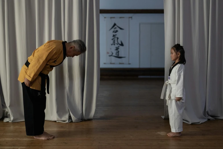 a man standing next to a little girl on a wooden floor, inspired by Kanō Tanshin, unsplash, shin hanga, with yellow cloths, grand master, still frame from a movie, back and standing