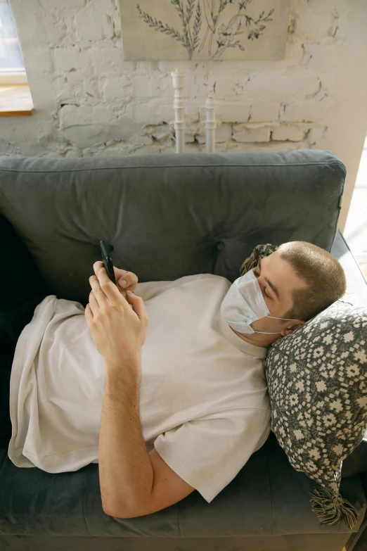 a man laying on a couch using a cell phone, pexels, happening, surgical mask covering mouth, instagram picture, grey, gif