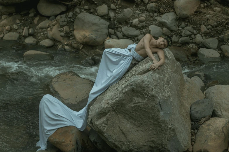 a woman laying on a rock in a river, inspired by Elsa Bleda, pexels contest winner, white gown, grey, standing on rocky ground, asleep