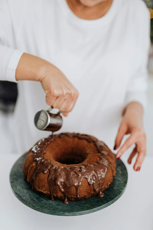 a woman sprinkles icing on a bundt cake, trending on pexels, made of liquid metal and marble, brown, grey, kek