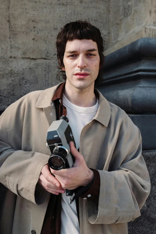 a man in a trench coat holding a camera, taken in the 2000s, young handsome pale roma, nathan fielder, medium format