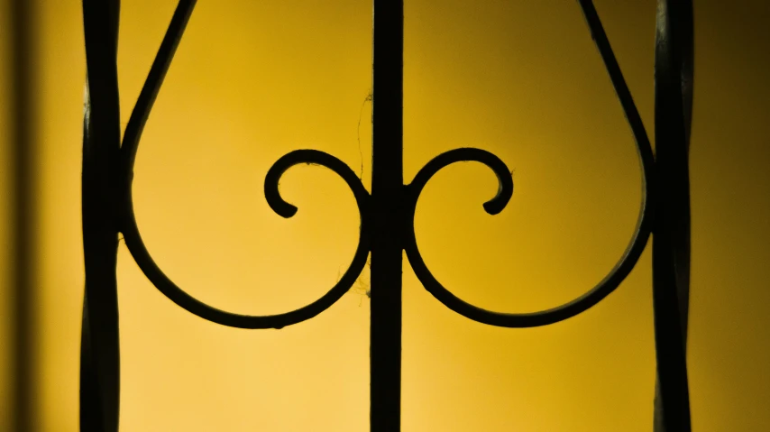 a close up of a wrought iron gate, an album cover, inspired by William Nicholson, flickr, yellow artificial lighting, yellow wallpaper, golden curve composition, emerging from a lamp