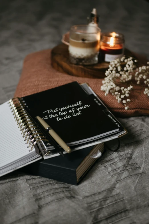 a stack of books sitting on top of a wooden table, writing in journal, white font on black canvas, pray, monthly