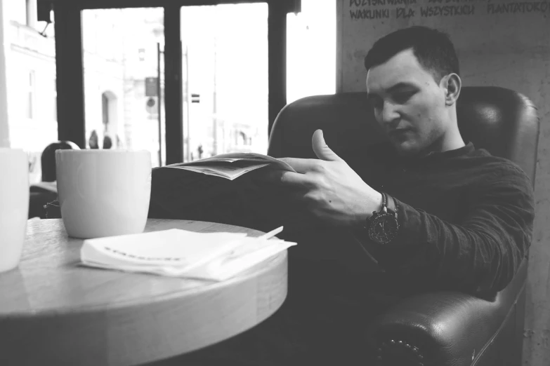 a man sitting at a table with a cup of coffee, by Mathias Kollros, pexels contest winner, luke evans, holding a book, hasbulla magomedov, sitting in a waiting room