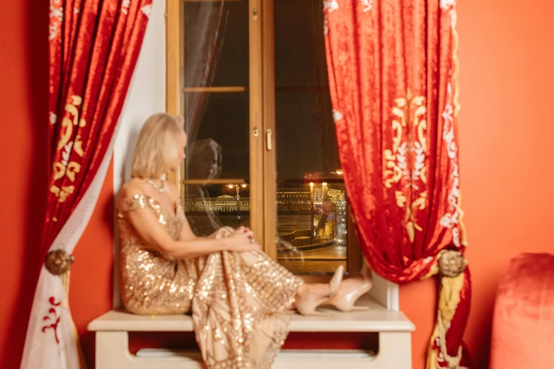 a woman in a gold dress sitting on a window sill, by Julia Pishtar, pexels contest winner, baroque, red curtains, at the terrace, a blond, gold and luxury materials