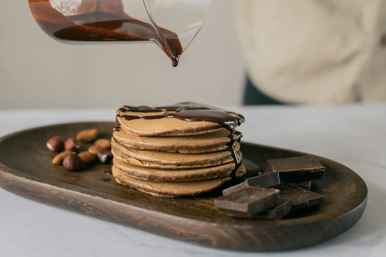 a person pouring syrup onto a stack of cookies, by Julia Pishtar, pexels contest winner, renaissance, fully chocolate, flat pancake head, natural wood top, glazed