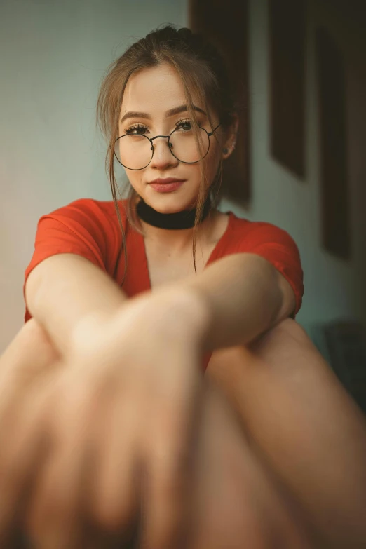 a woman with glasses sitting on the floor, a picture, trending on pexels, photorealism, hands behind her body pose!, red, asian features, selfie shot straight on angle