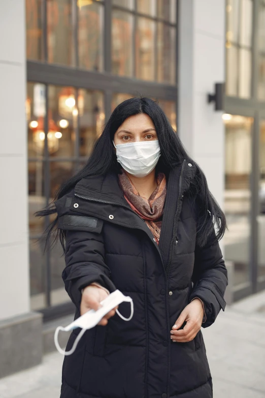 a woman wearing a face mask holding a video game controller, happening, walkable, delivering mail, standing in a city center, holding syringe