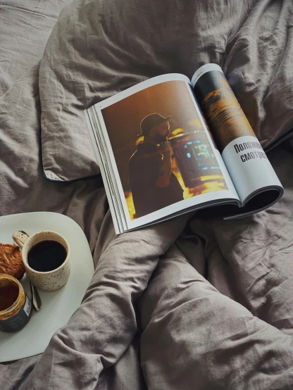 a book sitting on top of a bed next to a cup of coffee, by Lucia Peka, unsplash contest winner, photorealism, cover of a magazine, handsome, aykut aydogdu, magazine centerfold