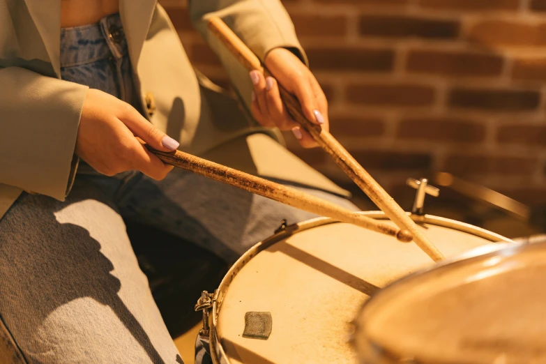 a woman playing drums in front of a brick wall, trending on pexels, warm light, brown, thumbnail, close up image