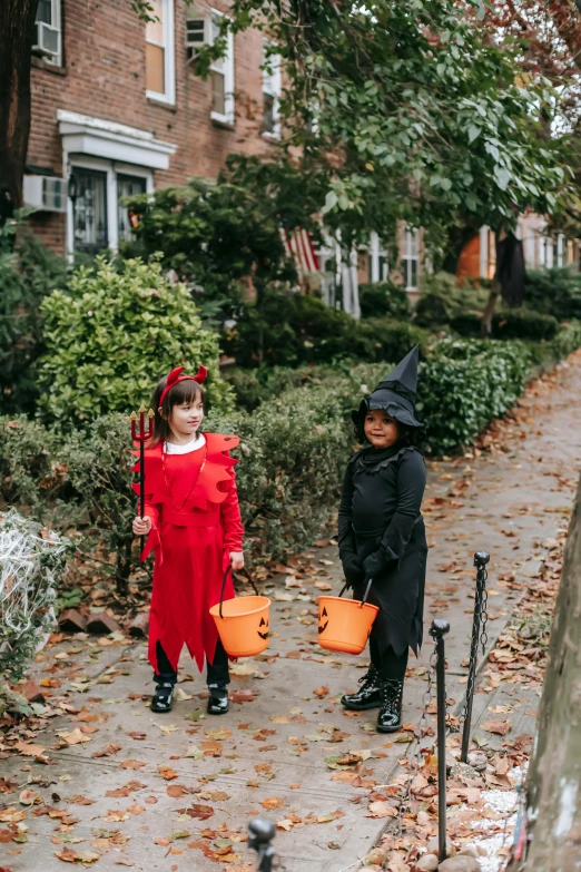 two children in halloween costumes walking down a sidewalk, a photo, pexels contest winner, brooklyn, a witch, red robes, gif