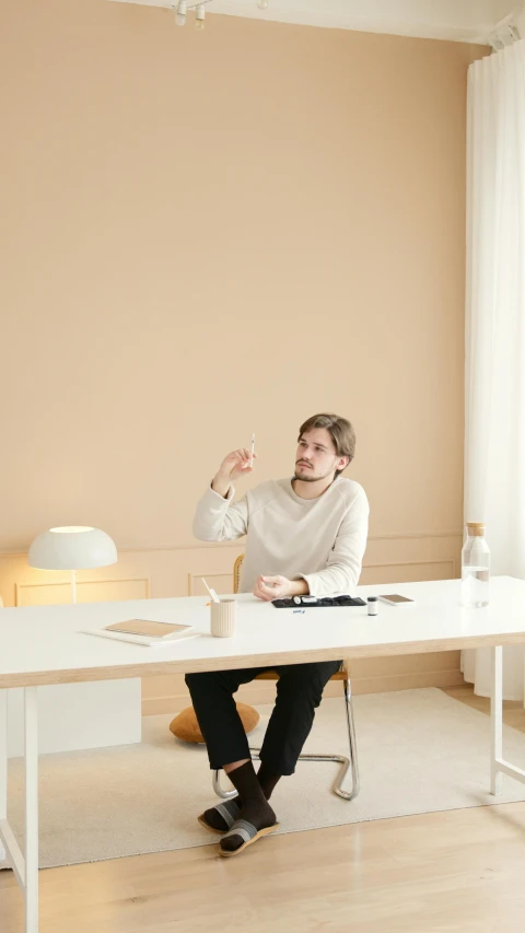 a man sitting at a desk in front of a window, a minimalist painting, inspired by Constantin Hansen, trending on unsplash, minimalism, cream - colored room, giving an interview, low quality photo, group sit at table