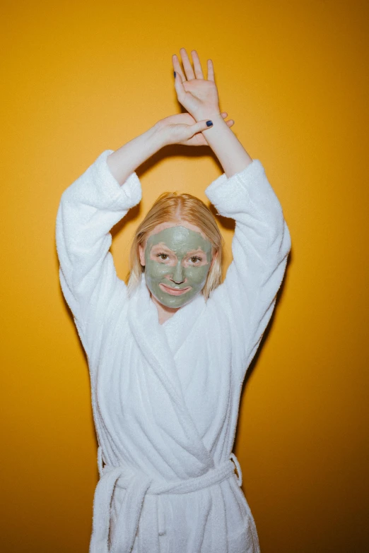 a woman in a bathrobe with a facial mask on, an album cover, inspired by Elsa Bleda, trending on pexels, happy face, green skin, ocher, a blond