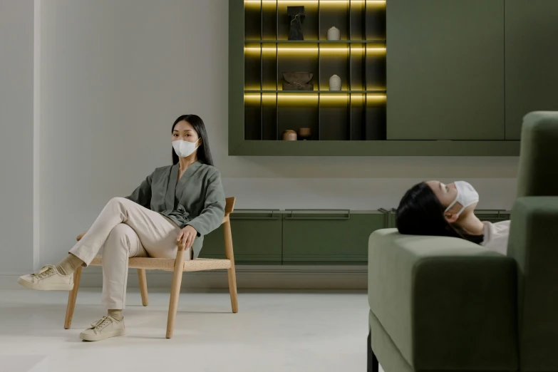 a woman sitting in a chair with a face mask on, inspired by Fei Danxu, minimalist furniture, 2 people, green facemask, **cinematic