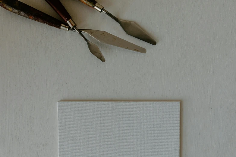 a couple of knives sitting on top of a piece of paper, a minimalist painting, inspired by Kyffin Williams, trending on pexels, white clay, card template, product introduction photo