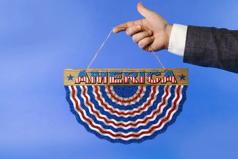 a person holding an american flag hanging from a string, inspired by Americo Makk, kinetic art, glowforge template, victorian arcs of sand, close up front view, trending on dezeen