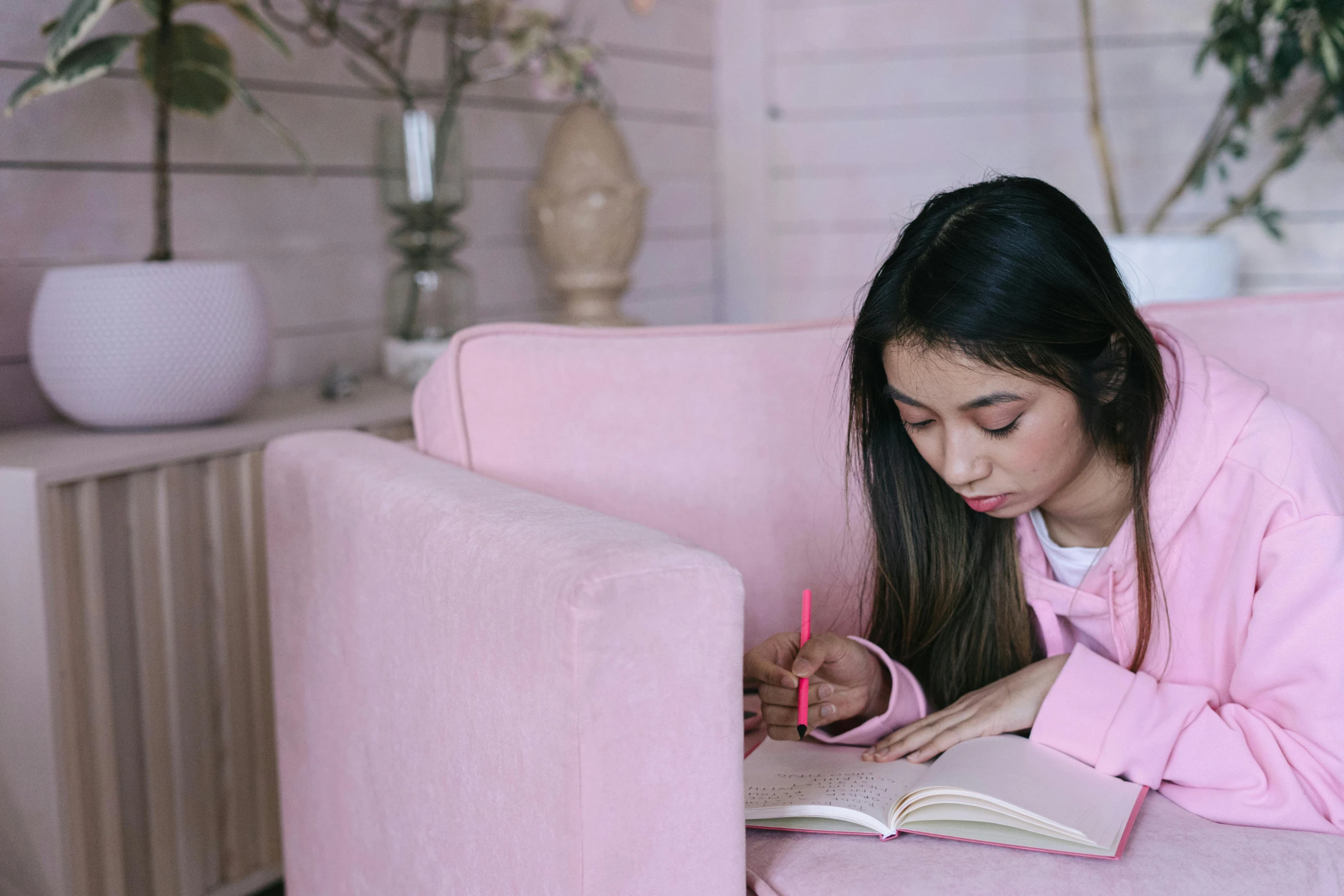 a woman reading a book on a pink couch, a drawing, pexels contest winner, school girl, writing in journal, girl wearing hoodie, wearing a light - pink suit