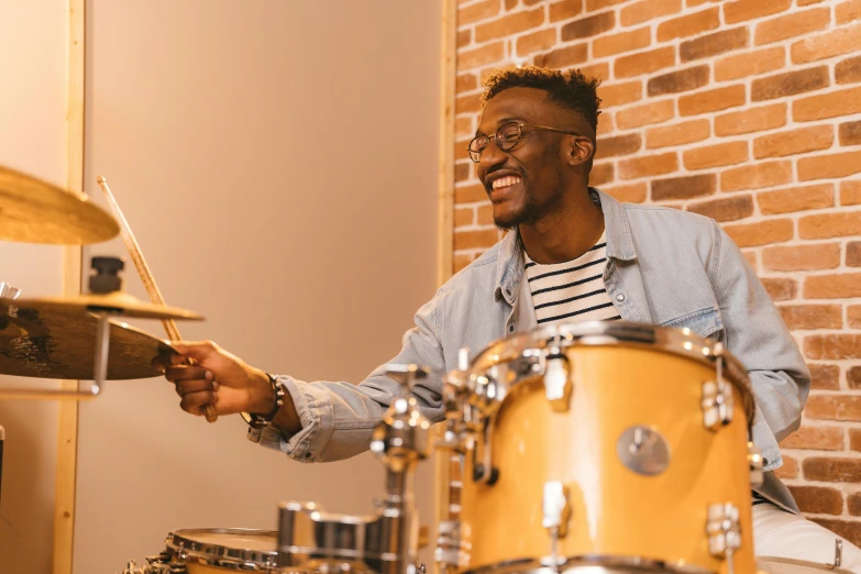 a man playing drums in front of a brick wall, pexels contest winner, black arts movement, brown skin man with a giant grin, nerdy music teacher with phd, at home, avatar image