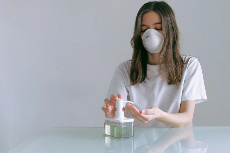 a woman sitting at a table with a bottle of hand sanitizer, by Adam Marczyński, pexels, renaissance, dust mask, with a white background, a person standing in front of a, wearing a cute top