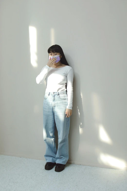 a woman standing against a wall talking on a cell phone, by Jang Seung-eop, instagram, baggy jeans, soft blue light, no face mask, white backdrop