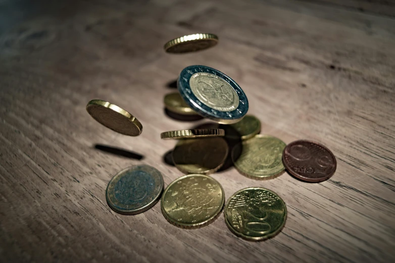 a pile of coins sitting on top of a wooden table, jumping towards viewer, colour photograph, mid shot, micro art