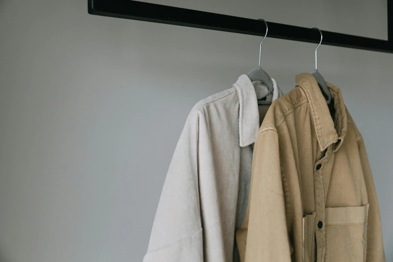 a couple of coats hanging on a rail, trending on pexels, minimalism, wear's beige shirt, utility, colour photo, uploaded