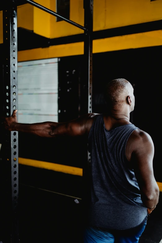 a man lifting a barbell in a gym, by Matija Jama, showing her shoulder from back, man is with black skin, headspace, thoughtful