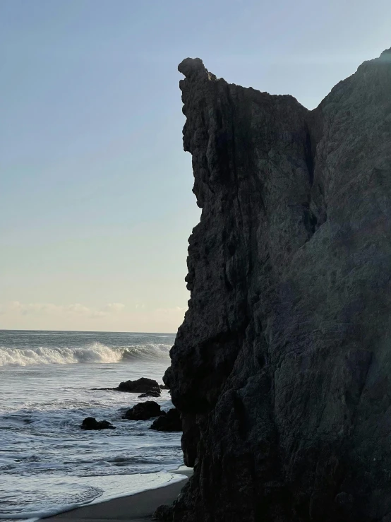 a large rock sitting on top of a beach next to the ocean, profile image, malibu canyon, ((monolith)), black sand