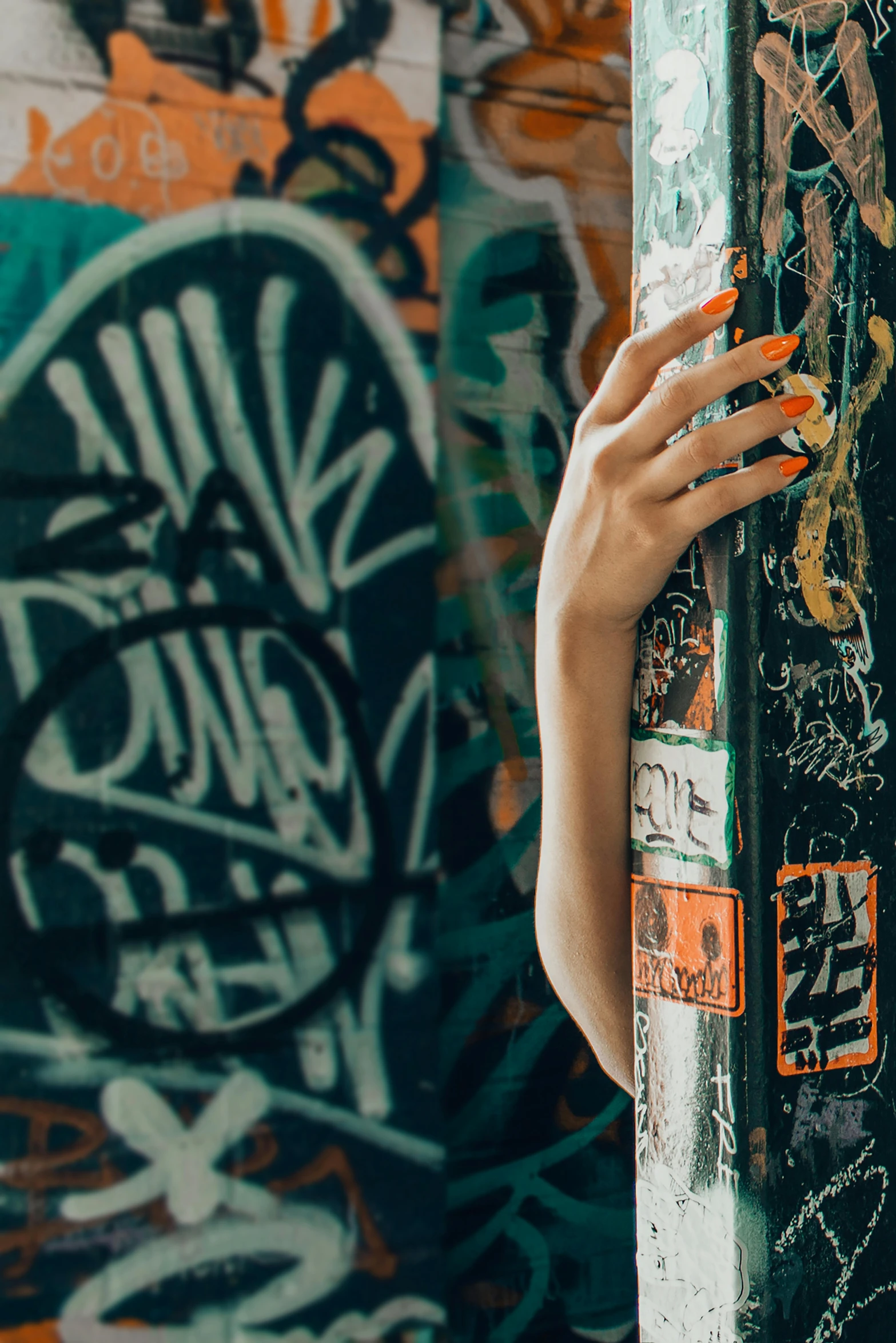 a woman standing in front of a graffiti covered wall, graffiti art, inspired by Elsa Bleda, trending on pexels, long nails, orange and black, half image, unclipped fingernails