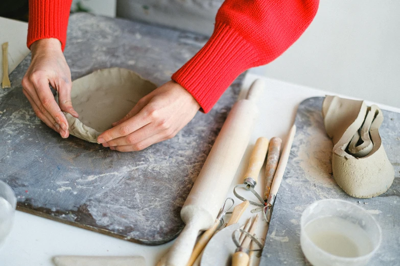 a woman is making a bowl out of clay, a still life, inspired by Sarah Lucas, grey, petite, ready - made, holding a baguette