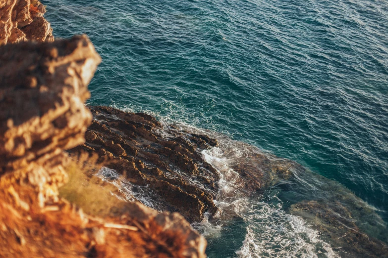 a person standing on top of a cliff next to the ocean, pexels contest winner, water texture, brown, alana fletcher, middle close up composition