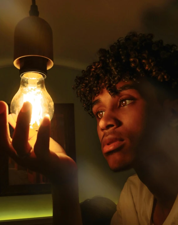 a man holding a light bulb in his hand, an album cover, pexels contest winner, black teenage boy, mood light, lgbtq, glowing jar