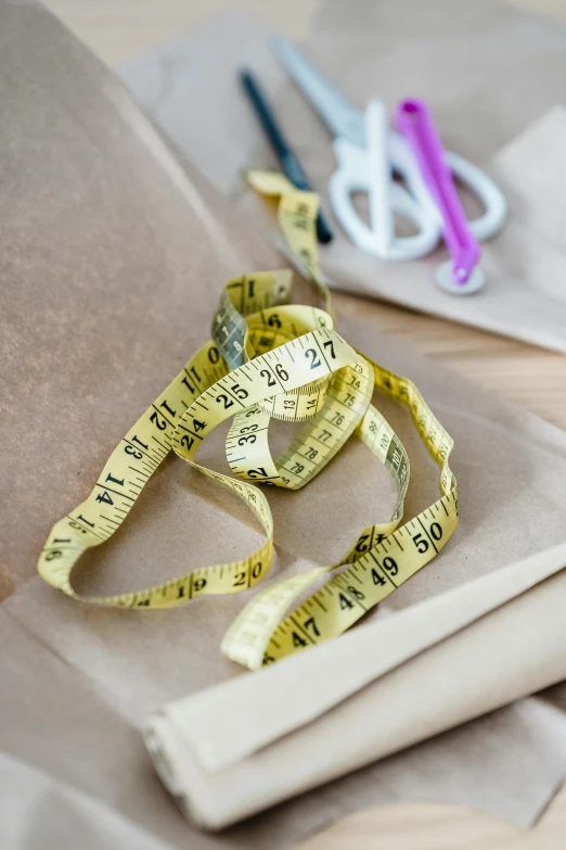 a pair of scissors and a measuring tape on a table, by Helen Stevenson, arts and crafts movement, dressed in red paper bags, plus-sized, yellowed paper, medium close up