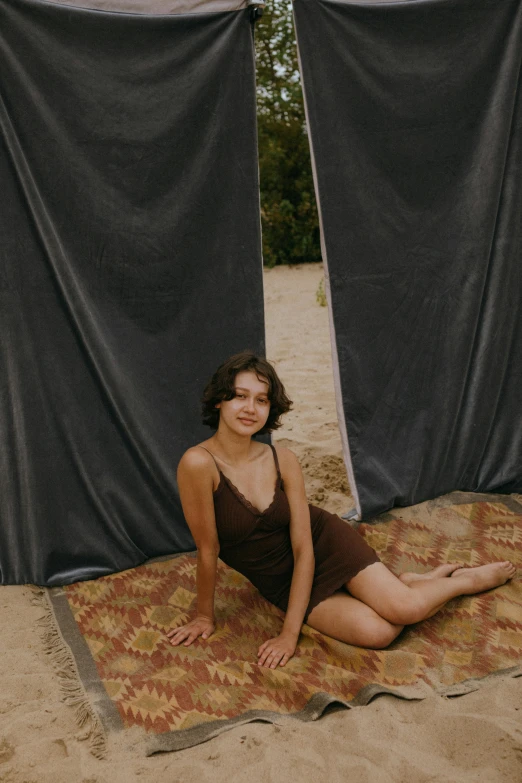 a woman sitting on a rug in the sand, an album cover, by Attila Meszlenyi, unsplash, renaissance, wearing a camisole and shorts, glamping, dark drapery, brown haired