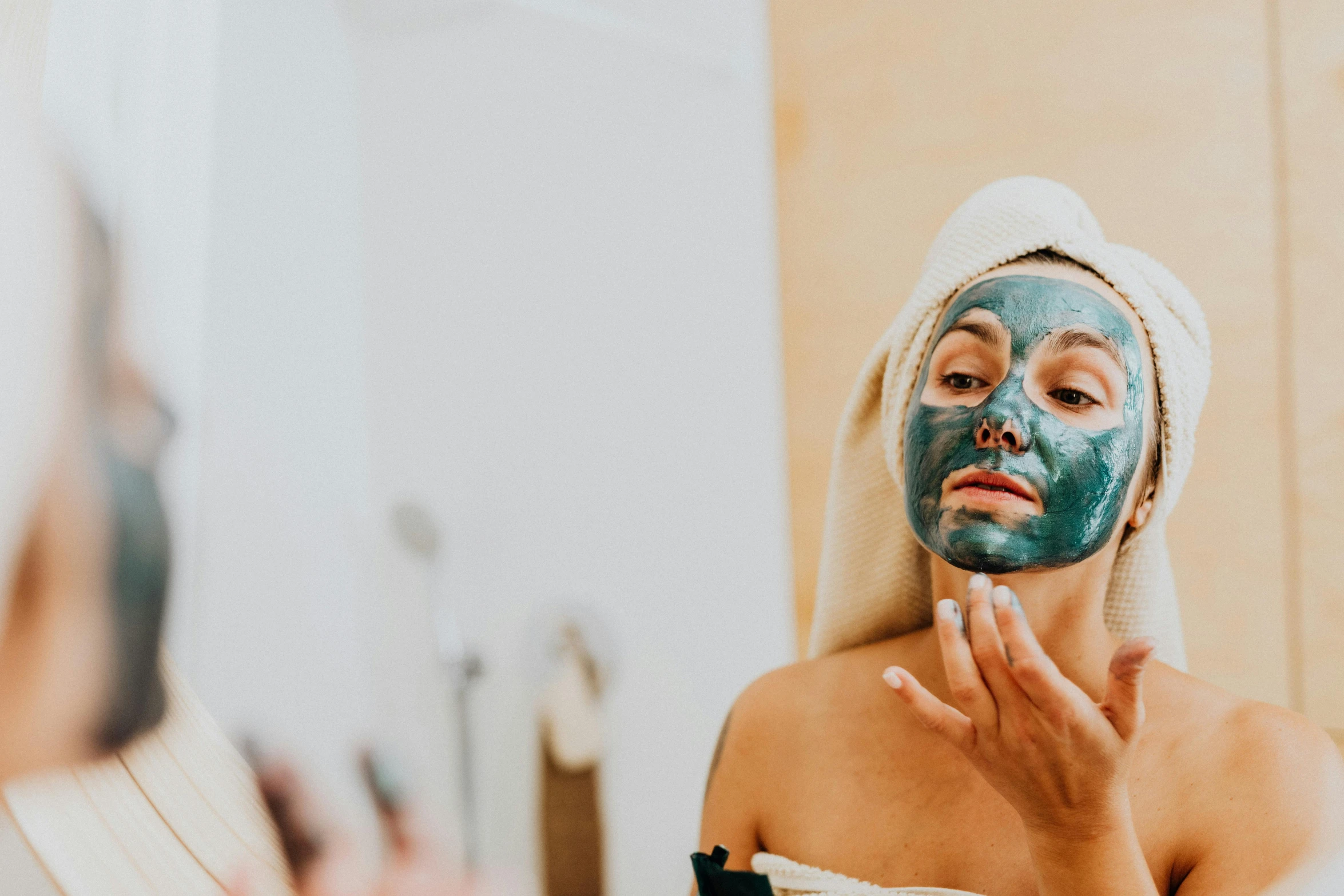 a woman wearing a face mask in front of a mirror, trending on pexels, teal skin, background image, manuka, wearing only a green robe