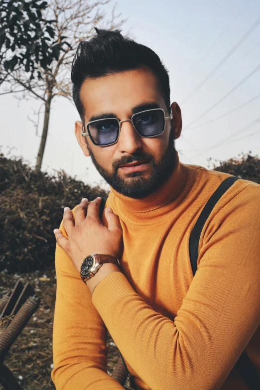 a man with a backpack posing for a picture, inspired by Manjit Bawa, trending on pexels, square rimmed glasses, he is wearing a brown sweater, coloured photo, male model