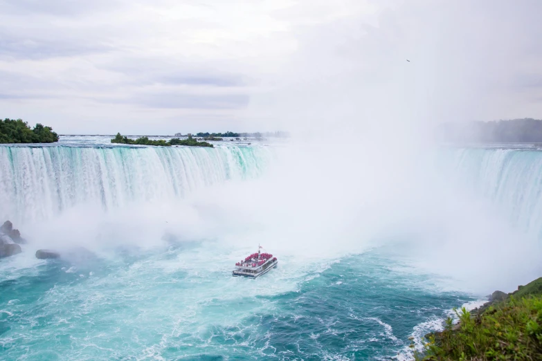 a boat that is in the water near a waterfall, by Julia Pishtar, pexels contest winner, hurufiyya, niagara falls, cn tower, conde nast traveler photo, ocean spray